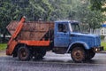 An old garbage truck rides in heavy rain