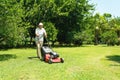 Old gardener with lawn mower in green garden. Royalty Free Stock Photo