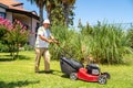 Old gardener with lawn mower in green garden. Royalty Free Stock Photo