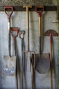 Old gardening tools including spades and forks hanging against a wall