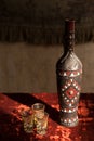 Old Georgian ceramic wine bottle with national ornament and three glasses on red velvet.