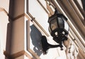 Old glass lantern in a black twisted frame on the white wall of the city building. Wall lamp on a Sunny day Royalty Free Stock Photo