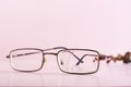Old glasses with a broken lens and a wire attached to the shackle on a pink background Royalty Free Stock Photo