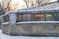 Old glasshouse with icicles covered with snow and ultraviolet lamps shining inside for plants growth