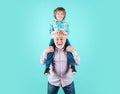 Old grandfather and young child grandson piggyback with funny face isolated on blue in studio. Granddad and cute boy
