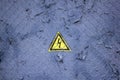 Old gray blue wall with peeling paint under a metal grid with a triangular yellow sign of dangerous electrical voltage. rough Royalty Free Stock Photo