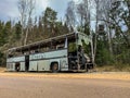 An old gray bus is abandoned on a road in the woods. Forest landscape with forgotten vintage gray bus. shattered commercial