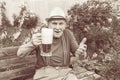 Old gray-haired man in a hat with a glass of beer in the garden. A man drinks beer on vacation. Tinted in sepia Royalty Free Stock Photo