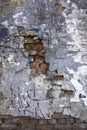 Old gray heavily damaged concrete wall with deep relief and protruding red bricks, cracks and various stains of paint and dirt. Royalty Free Stock Photo