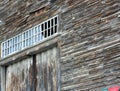 Old gray siding of old wooden barn peeling aound transom window above barn doors