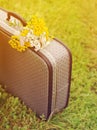 Old gray suitcase and bouquet of yellow wild flowers on a green grass in summer sunny day.