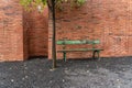 An old green bench stands next to a green tree in front of a brick wall on a stone chipping background Royalty Free Stock Photo