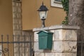 An old green mailbox hangs on a stone fence near an old street lamp. Soviet mailbox. A place to store mail Royalty Free Stock Photo