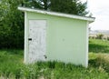 Old green painted wood storage shed on a farm showing front facing, slanted roof and white door. Royalty Free Stock Photo