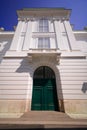 Old green wooden doors closed. Facade of baroque white building with balcony, pilasters and cornice