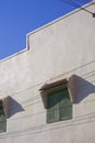 The old green wooden window on vintage white house wall with cable lines against blue clear sky Royalty Free Stock Photo