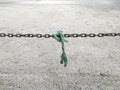 Old green worn rope tied in rusty chain horizontally on dirt ground. Old nylon rope hanging on rusty chain links Royalty Free Stock Photo