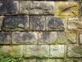 Old grey damp stone wall made of large regular blocks covered in patches of moss