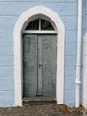old grey door with a white arched frame in a brick wall painted in blue