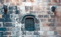Old grilled window in brick stone wall of castle photo. Urban scenery photography with fortress side wall. Royalty Free Stock Photo
