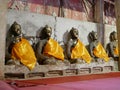 Old grungy Buddha statues sitting in a row with glossy yellow monk robes