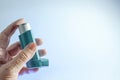 Old hand holding a meter-dosed inhaler, also known as pump or allergy spray, medical device for asthma or COPD patients, light