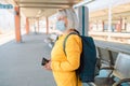 Old happy woman in a face mask with backpack waiting train on station platform with big bag, passport and ticket on Royalty Free Stock Photo