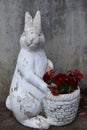 Old hare figure in front of the concrete wall holding a basket of flowers.