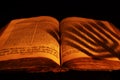 Old Hebrew Bible in light of burning candle on dark background. Shadow from menorah on open Jewish prayer book. Closeup Royalty Free Stock Photo