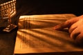 Old Hebrew Bible and silver menorah in light of burning candle on dark background. Shadow from menorah on open pages