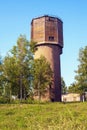 An old high brick water tower with a wooden plank annex on top in the rays of the rising sun among the grass and trees Royalty Free Stock Photo