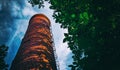 Old high chimney of a boiler room made of red bricks without smoke against a blue sky with dark clouds and green foliage. Bottom Royalty Free Stock Photo