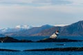 Old historic light house on the coast of Norway on clear sunny winter day with snow capped mountains in background Royalty Free Stock Photo