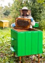 Old hiver in protective suit with hive frame