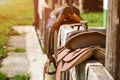 Old horse saddle placed on wooden fence next to house, lit by sun. Royalty Free Stock Photo
