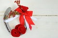 An old horseshoe decorated with red roses made of felt with red and white ribbons on a white washed rustic wooden background.