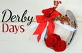 An old horseshoe decorated with red roses made of felt with red and white ribbons on a white washed rustic wooden background.