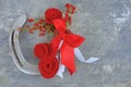 An old horseshoe decorated with red roses made of felt with red and white ribbons on a worn and scratched steel background.