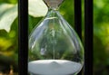 Old hourglass with transparent glass flask on blurred green nature background. Glassy sandglass in black wooden case Royalty Free Stock Photo