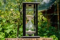 Old hourglass on wooden deck on a blurred background of a green garden. Glass sandglass in black wooden case with white Royalty Free Stock Photo