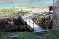 Old improvised homemade partially broken rusted metal bridge over narrow water canal surrounded with stones and green grass