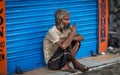 Old Indian beggar sits in front of a closed shop and has a cup of morning tea on a road in South Kolkata, West Bengal, India.