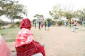 An old indian lady sitting on the bench and watching children playing in an open gym in a park Royalty Free Stock Photo