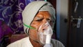 Old Indian man infected with Covid 19 disease. Patient inhaling oxygen wearing mask with liquid Oxygen flow