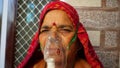 Old Indian woman infected with Covid 19 disease. Patient inhaling oxygen wearing mask with liquid Oxygen flow
