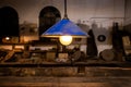 Old industrial electric lamp light turned on with glowing bulb only in focus. Blue shade, workbenches and tools