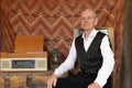 An old intelligent man in white shirt sitting near old radio at home. Retirement. Retro style Royalty Free Stock Photo