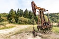 Old iron rusty oil derrick pump in work on the lawn among green trees in summer. Horizontal orientation.