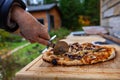 Old lady is cutting a pizza that just came out of an outdoor bread oven