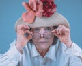 Mature woman with glasses and a hat looks straight into the eyes.Isolated against blue background Royalty Free Stock Photo